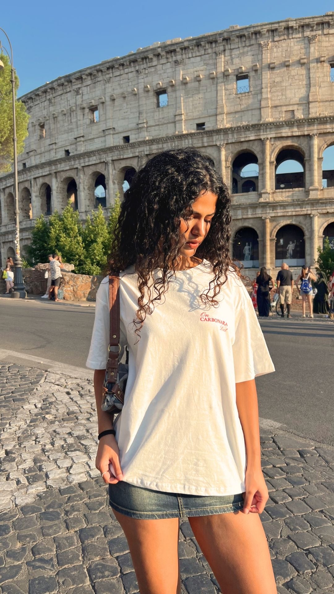 Woman standing in front of the Colosseum in Rome, wearing a white t-shirt and denim shorts.
